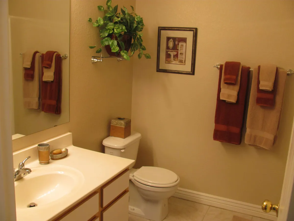 A comfortable and stylish bathroom scene with a bright sink area, large mirror, plush towels, a touch of greenery, and tasteful framed art. The atmosphere feels spa-like and well cared-for, offering a sense of serenity and hygiene.