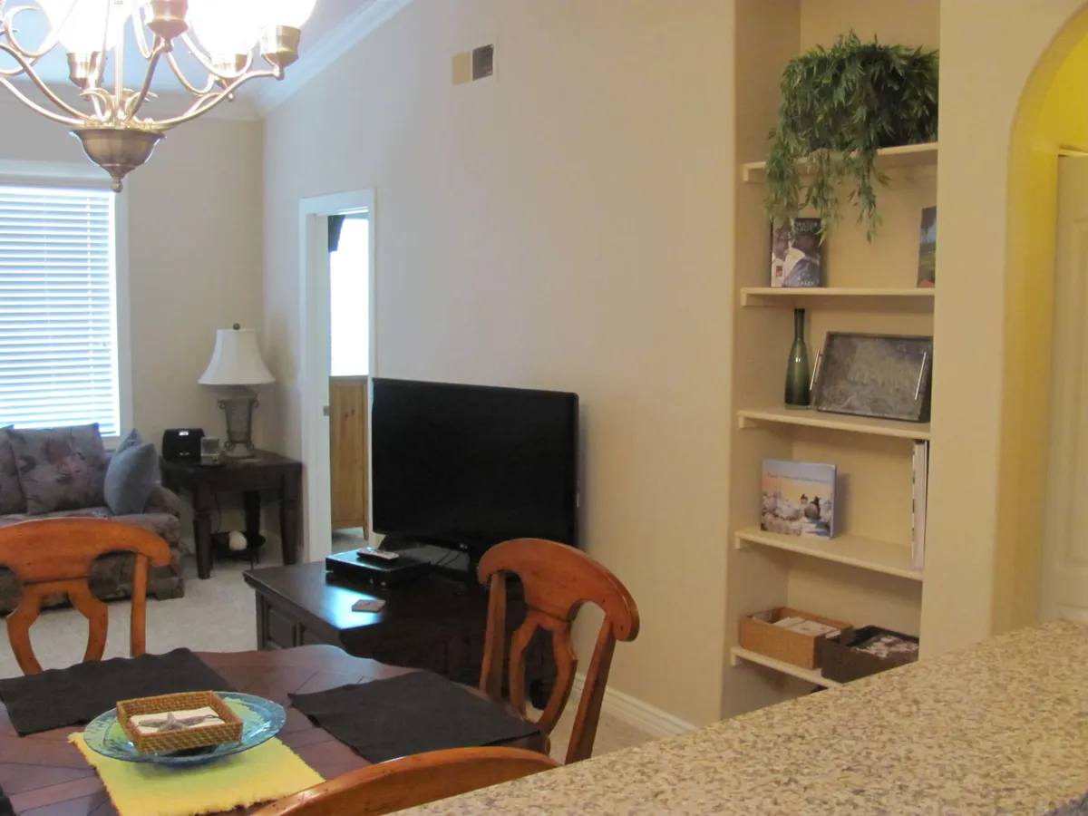 This image showcases a warm and welcoming living room with a stylish dining table and chairs, a comfortable sofa, television, and neatly arranged shelves with decorative items. The space is filled with natural light, creating an inviting atmosphere that complements the idea of a sanctuary.