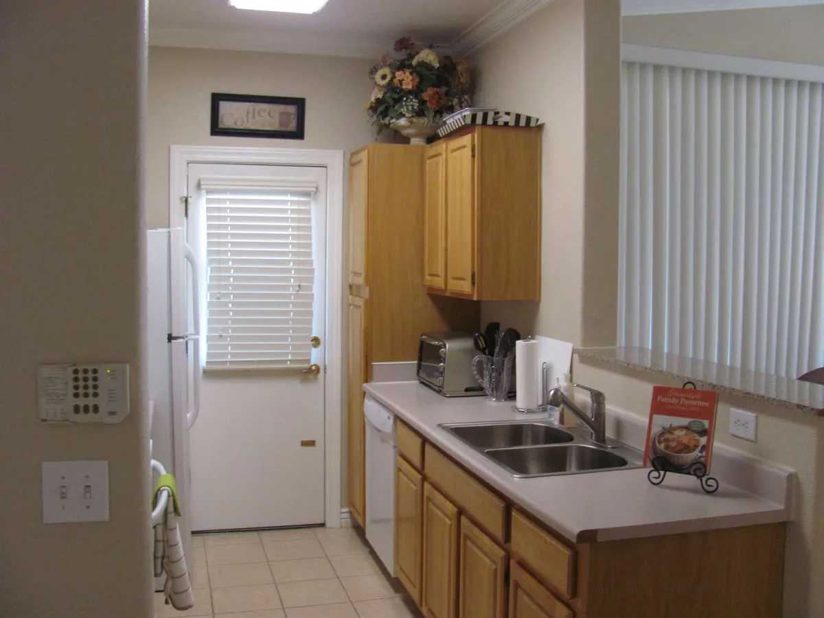 A bright, welcoming kitchen space featuring a large sink, rows of kitchen cabinets, and a door leading outside. Natural light fills the room, suggesting easy access between indoor comfort and outdoor fun, perfect for gatherings or family meals.