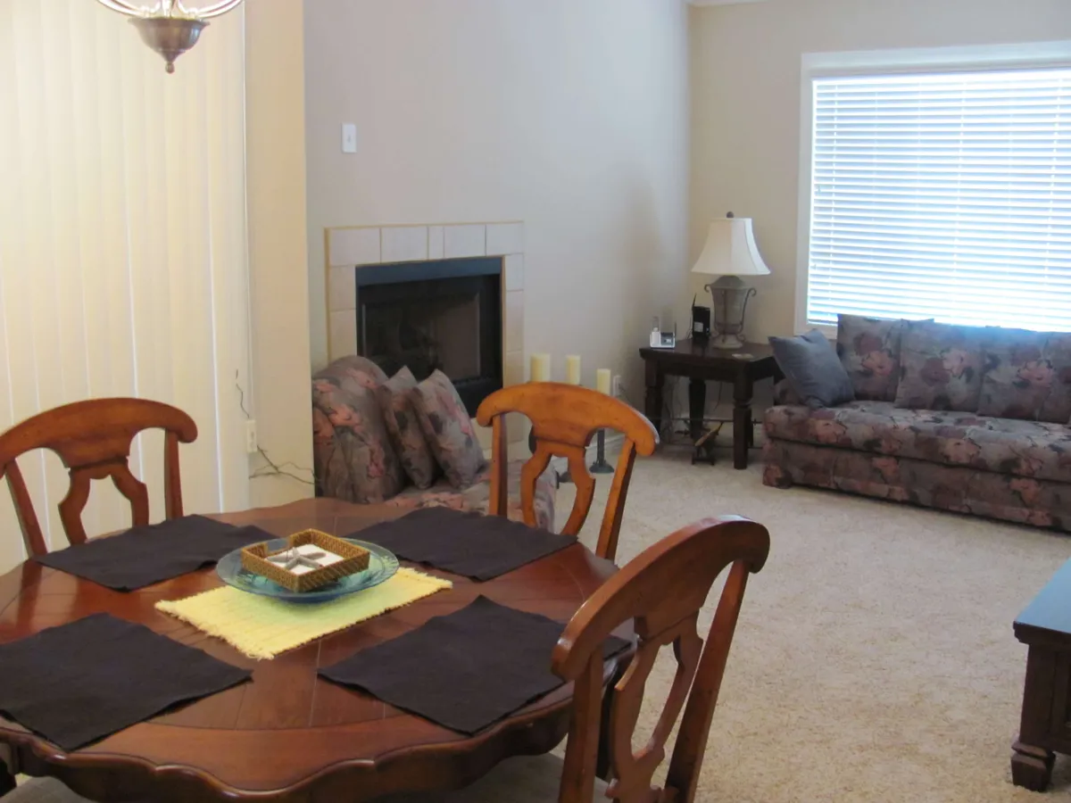 This image displays a living and dining area with a central fireplace, a comfortable sofa, and a dining table set for shared meals. The inviting mood is enhanced by warm lighting and thoughtful design elements.