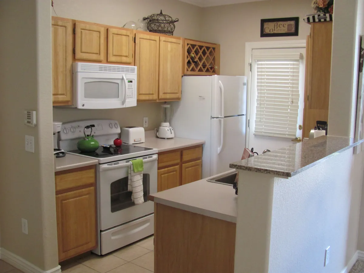 A cozy kitchen scene featuring a countertop with small appliances, a stove with a cheerful green kettle, and classic wooden cabinets. The setup emphasizes functionality and the pleasures of cooking or baking at home.